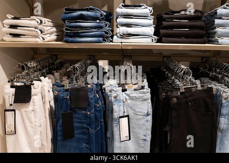 Pile di jeans blu disposte ordinatamente su scaffali di legno in un negozio di abbigliamento, che espone la moda al dettaglio e il concetto di merchandising Foto Stock