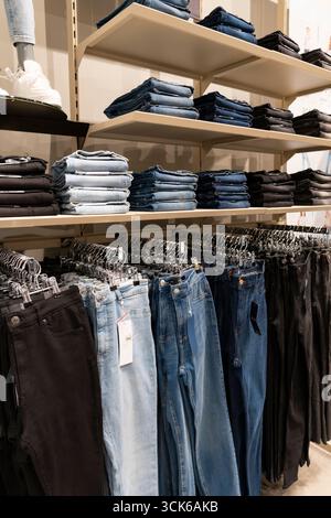 Pile di jeans blu disposte ordinatamente su scaffali di legno in un negozio di abbigliamento, che espone la moda al dettaglio e il concetto di merchandising Foto Stock