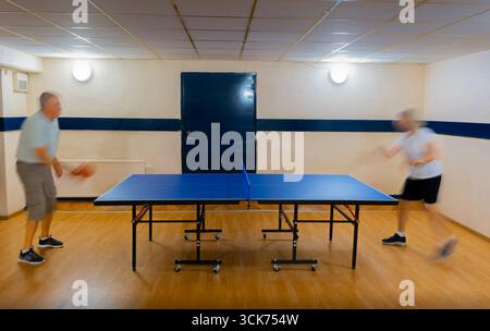Due persone anziane che giocano a ping-pong in una cantina. Movimento sfocato Foto Stock