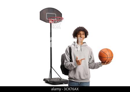 Sorridente ragazzo afroamericano che tiene una pallacanestro e punta isolato su sfondo bianco Foto Stock