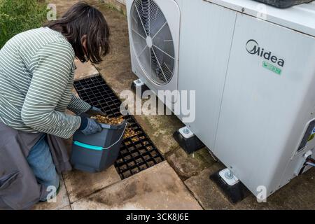 Donna che crea un soakaway di fronte a una pompa di calore Midea per fornire uno scarico per la condensa. Foto Stock