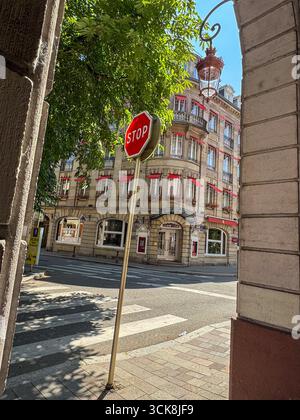 Strada francese con segnale di stop rosso, edificio classico in pietra, tende rosse, balconi in ferro battuto e pedonale all'incrocio zebra. Foto Stock