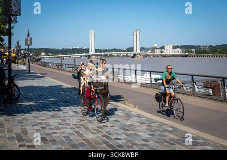 Una donna con i suoi figli in bicicletta vicino al fiume Garonna e al ponte Jacques Chaban Delmas a Bordeaux, Francia. Foto Stock