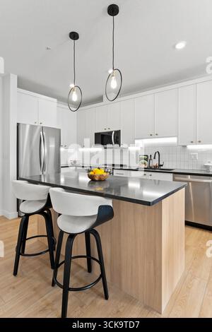 Cucina con un bancone e due sedie. Le sedie sono bianche e il bancone è nero. C'è una ciotola di frutta sul bancone Foto Stock