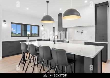 La cucina è spaziosa e ha una grande isola con un lavandino e un rubinetto. Ci sono sedie nere intorno all'isola e una finestra sopra il lavandino. Il ki Foto Stock