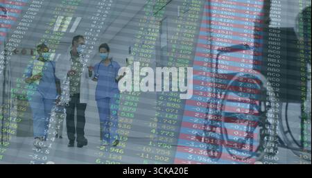 Squadra medica che cammina indossando camice da laboratorio, scrub e maschere lungo il corridoio dell'ospedale, con copertura stock Foto Stock