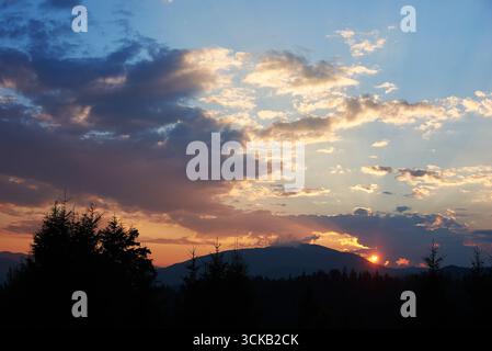 Sereno cielo serale con sfumature di blu e rosa tenue al tramonto. Horizon si illumina delicatamente, illuminando alberi di pino e colline ondulate, creando un paesaggio tranquillo ed esteso. Foto Stock