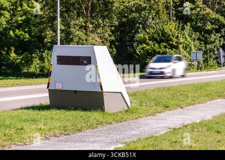 Un'auto in corsa sta per passare davanti a un autovelox mobile posto sul lato di una strada trafficata per le forze dell'ordine del traffico in una piccola città in Francia. Foto Stock