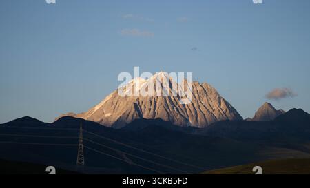 La luce del sole dorata illumina le aspre creste della montagna innevata di Yala all'alba a Garzê, Sichuan. Foto Stock
