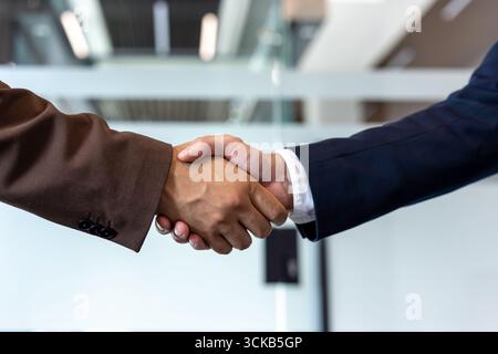 Due uomini d'affari stanno stringendo la mano dopo aver raggiunto un accordo durante una riunione produttiva in un ufficio moderno, simboleggiando la partnership e il successo Foto Stock
