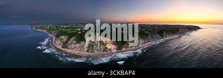 Vista aerea delle scogliere spettacolari incontra il mare buio e slancinante sotto un cielo che si illumina con le sfumature ardenti del tramonto, New Shoreham, Rhode Island, Stati Uniti. Foto Stock