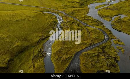 Immagine aerea di una strada tortuosa attraverso il terreno coperto di muschio in Islanda, con ruscelli, fiumi e una piccola cascata in un ambiente rurale remoto. Foto Stock