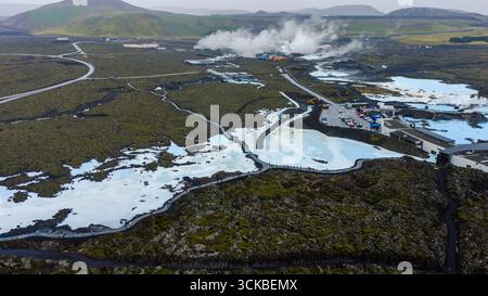 Le acque azzurre lattiginose della Laguna Blu contrastano con i campi di lava scura, il vapore che sale da una pianta geotermica e i sentieri in mezzo al terreno vulcanico. Foto Stock