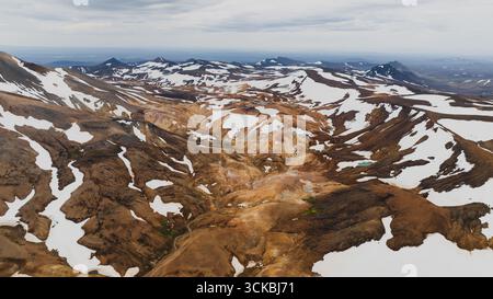 Spettacolare vista aerea delle colorate montagne riolite di Landmannalaugar, con colori vivaci, macchie di neve, valli e vette lontane sotto un cielo nuvoloso. Foto Stock