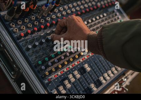Primo piano di una mano che regola le manopole su una console di mixaggio audio, con pulsanti e manopole colorati Foto Stock