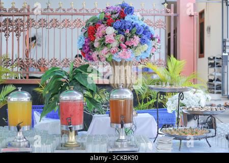 Un tavolo a buffet splendidamente organizzato caratterizzato da colorate composizioni floreali, distributori di bevande con bevande e un assortimento di antipasti Foto Stock