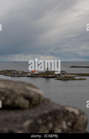 Un piccolo insediamento norvegese su un isolotto roccioso presenta edifici modesti, una struttura dal tetto rosso e una torre di pietra, circondata da acque calme e un'area di Foto Stock