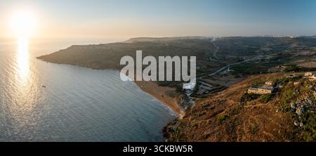 Vista aerea della luce dorata del sole che baciano le tranquille acque turchesi che incontrano la spiaggia sabbiosa di Ramla Beach, Gozo, Malta. Foto Stock