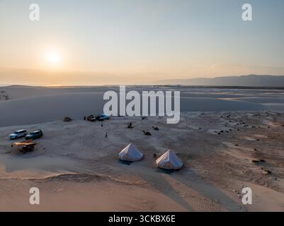 Vista aerea delle tende piazzate sulle dune di Steroh sotto un'alba dorata, che proietta lunghe ombre attraverso il paesaggio arido, le dune di Steroh, Socotra, Yemen. Foto Stock