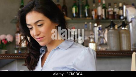 Guardando verso il basso il barista in piedi dietro il banco di legno nel caffè, con peonie rosa, spazio per copiare. Rustico, elegante, professionale, senza tempo, caldo, invito Foto Stock