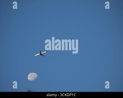 Aereo di linea di medie dimensioni che passa vicino a una luna quasi piena con un cielo azzurro. Foto Stock