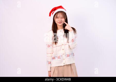 bella donna sorridente in cappello babbo natale con maglione festivo che celebra le festività natalizie con sfondo bianco in studio natalizio Foto Stock