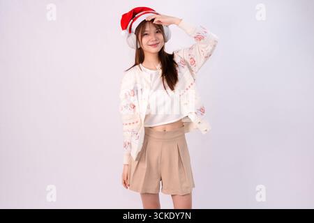bella donna sorridente che festeggia il natale indossando cappello di babbo natale e cuffie con sfondo bianco Foto Stock