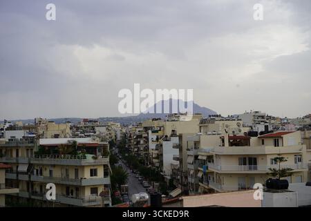 Una vista elevata del fitto paesaggio urbano di Heraklion con una montagna in un giorno coperto, che offre uno sguardo sulla vita della città dell'isola. Foto Stock