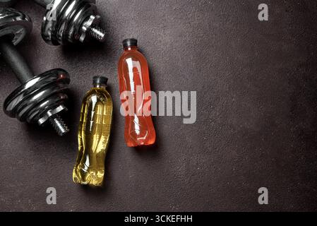 Bevanda sportiva isotonica con manubri (barcampanelli) su sfondo scuro, vista dall'alto, spazio copia. Elettrolita bevanda fitness, concetto di stile di vita sano. Foto Stock
