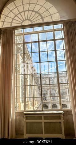 Vista attraverso una grande finestra ad arco con tende, che mostra l'architettura classica e il cortile del Palazzo reale di Madrid, Spagna. Foto Stock