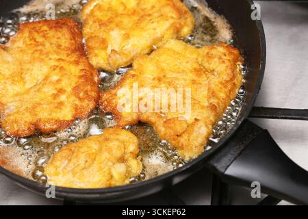 Cotolette di carne fritte dorate in padella. Processo di cottura con olio caldo. Superficie croccante. Preparazione tradizionale del cibo fatto in casa. Primo piano del pasto appena fritto. Foto Stock