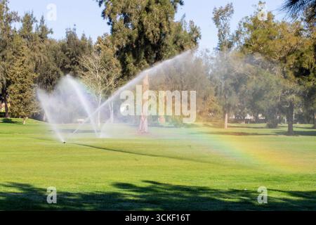 Innaffiare il fairway sul campo da golf con grandi spruzzi d'acqua che creano un arcobaleno Foto Stock