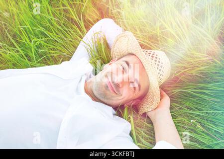 Giovane con cappello di paglia disteso contento su un prato Foto Stock