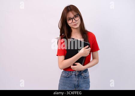 donna sorridente che tiene in mano il notebook con eleganti occhiali e un abito rosso sullo sfondo dello studio Foto Stock