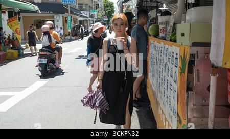 Tainan, Taiwan 7 settembre 2025: La donna beve il tè al latte nel mercato. Da un famigerato passato a un paradiso gastronomico di oggi, l'iconica parete di Yongle si erge Foto Stock
