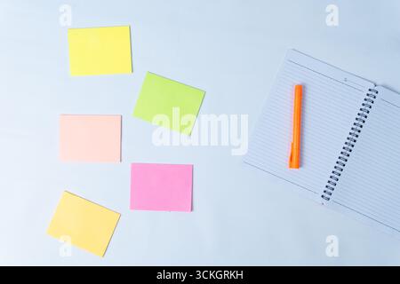 Appunti colorati disposti su una scrivania bianca con un notebook aperto e un pennarello arancione, che simboleggiano l'organizzazione, la pianificazione, i promemoria e la produttività. Foto Stock