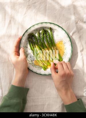 Immagine piatta di un paio di mani con un piatto di asparagi, asparagi officinali e salsa hollandaise Foto Stock