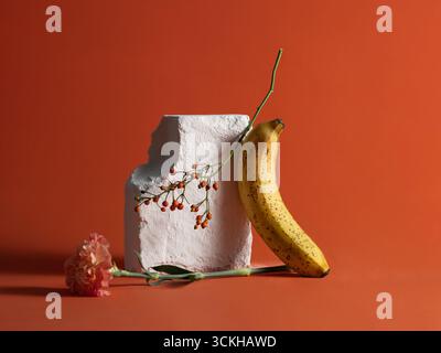 Una natura morta elegante con banana matura, fiori e frutti di bosco Foto Stock