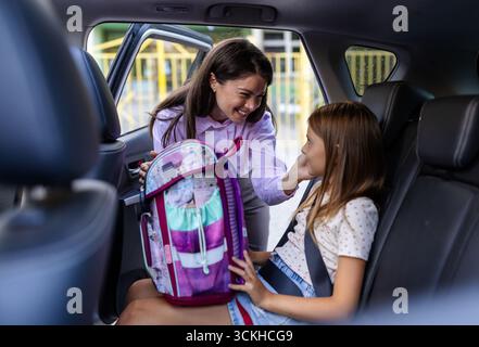 La madre sorride a sua figlia sul sedile posteriore, che tiene in mano lo zaino della scuola. L'ambiente è un pomeriggio caldo Foto Stock