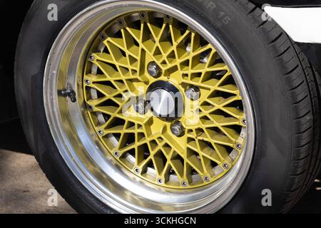 Cerchi in lega d'oro lucido dal design intricato delle razze, montati su un pneumatico per auto d'epoca, che mette in risalto l'estetica automobilistica d'epoca Foto Stock