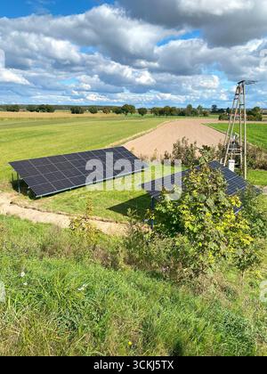 Pannelli solari installati su terreni agricoli aperti con un paesaggio rurale chiaro sullo sfondo. L'impianto rappresenta la produzione di energia rinnovabile e ce Foto Stock