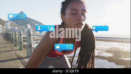 Donna pendente in cima rosa che si affaccia sul lungomare mostrando icone fluttuanti dei social media Foto Stock