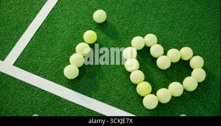 Mostra palle da tennis gialle che formano la forma del cuore sull'angolo del campo da tennis, con linee bianche Foto Stock