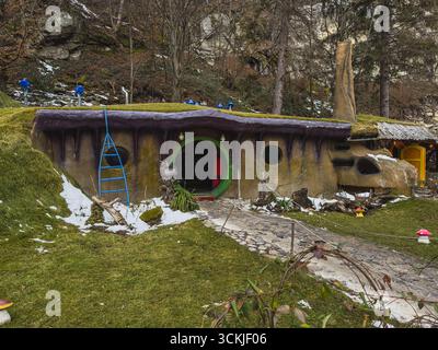 Una casa stravagante con caratteristiche vibranti si trova in mezzo a una foresta innevata. L'erba verde e la neve sparsa creano un ambiente invernale sereno, completato da tre Foto Stock