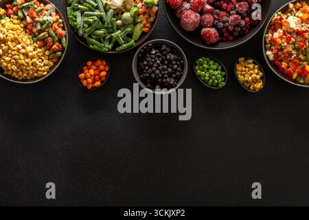 Una varietà di verdure e frutta congelate disposte in piatti, su sfondo scuro, catturando l'essenza della conservazione estiva per i pasti invernali Foto Stock
