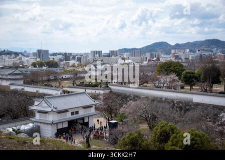 Giardini del castello di Himeji con vista sulla città sullo sfondo. Vista dei giardini del castello di Himeji con porte, mura e città moderna sullo sfondo. Foto Stock