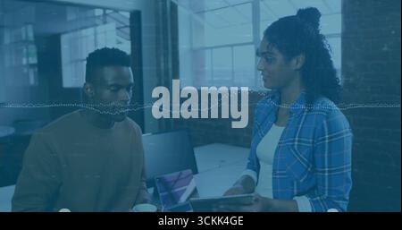 Colleghi che discutono i dettagli del progetto in un ufficio moderno, con notebook, tablet e tazza da caffè Foto Stock