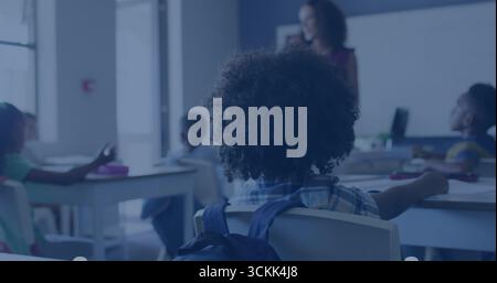 Bambino con capelli ricci e zaino blu seduto di fronte all'insegnante in classe, lavagna bianca Foto Stock