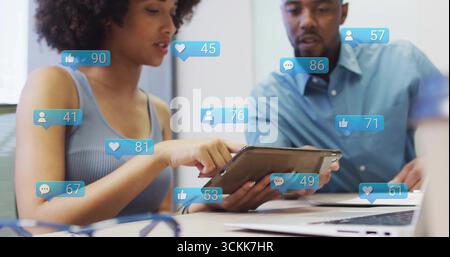 Collaborare con due colleghi in abiti da lavoro che esaminano il tablet in ufficio, con sovrapposizioni fluttuanti Foto Stock