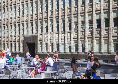 Londra, Regno Unito - 27 giugno, 2025 - persone che godono del caldo clima estivo in uno spazio all'aperto con l'edificio per uffici Holland House sullo sfondo Foto Stock
